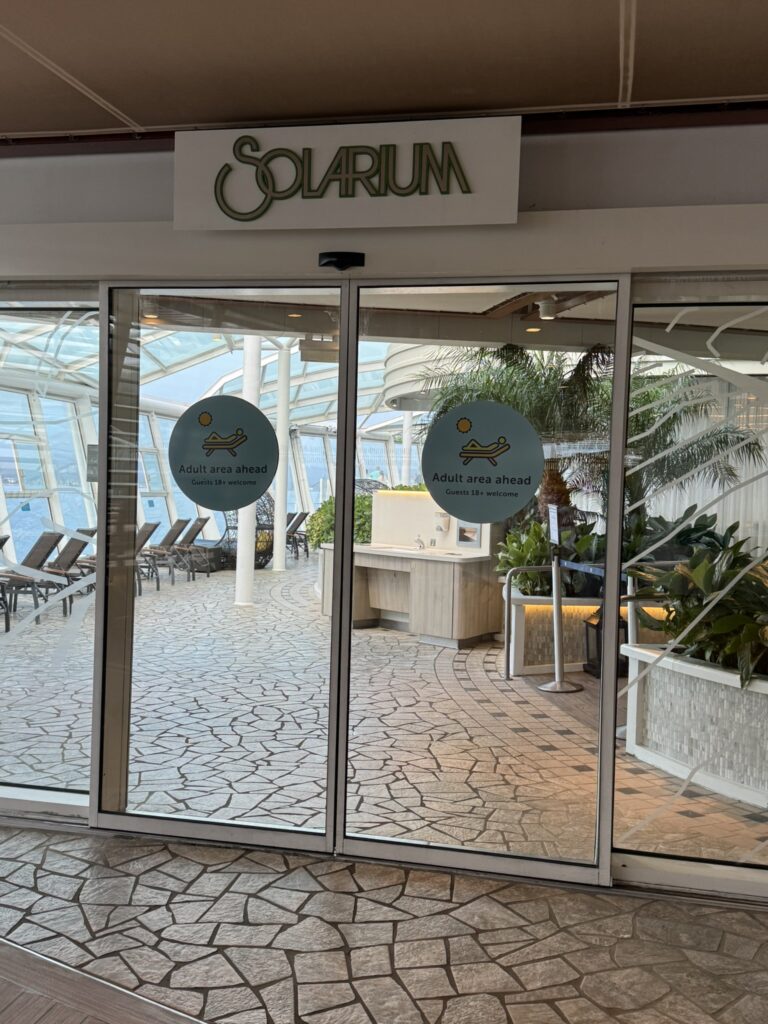 Entrance to the adults‑only solarium on a cruise ship, with glass doors, tropical plants, and signage indicating the 18+ relaxation area.
