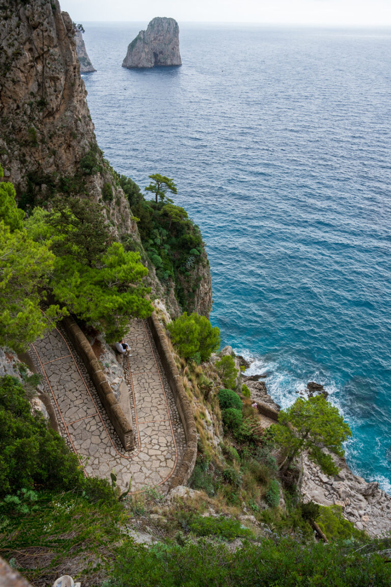 View looking down on a winding stone path in Capri descending a steep cliffside toward the turquoise Mediterranean Sea