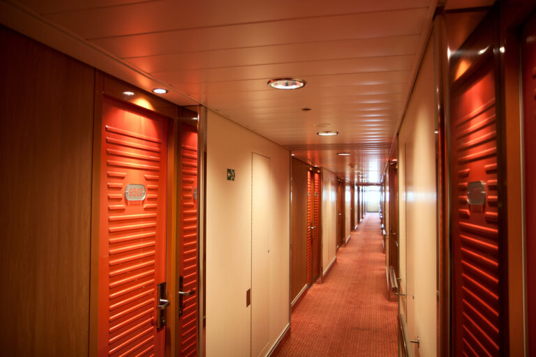 Cruise ship hallway lined with stateroom doors, showing how to choose your stateroom based on location and layout.