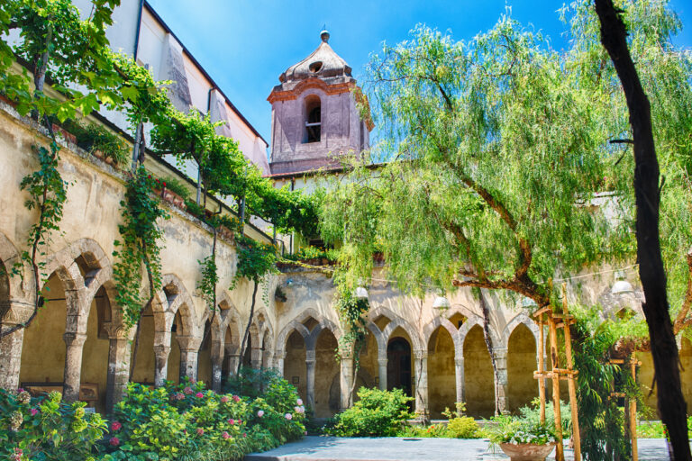 Sunlit courtyard of the Cloister of San Francesco in Sorrento with medieval arches and lush greenery