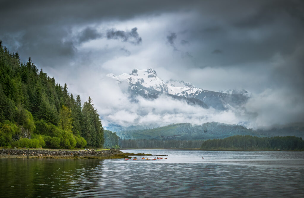 Forest‑covered shoreline and mountain views along the Icy Strait near Hoonah, Alaska, with distant coastal scenery beneath low clouds.