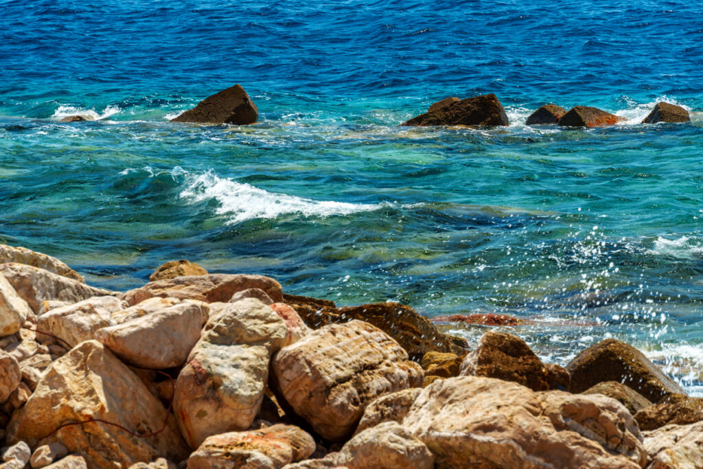 Rocky coastline with turquoise and deep blue water crashing against shoreline rocks, reflecting the natural beauty of Grand Turk’s western coast.