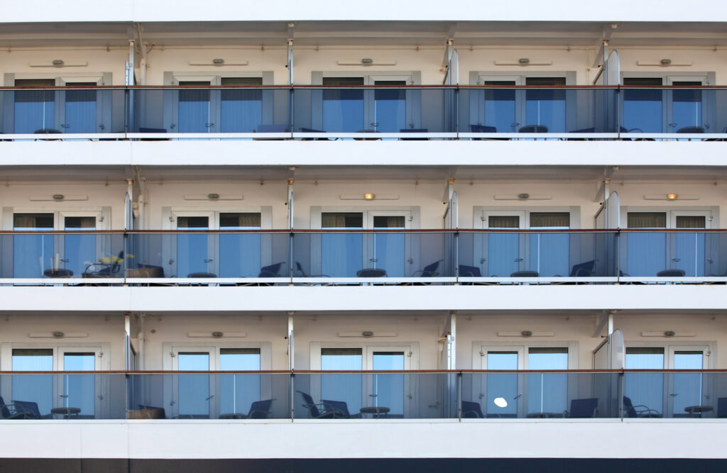 Row of cruise‑ship balcony staterooms with glass railings and outdoor seating arranged across multiple decks.