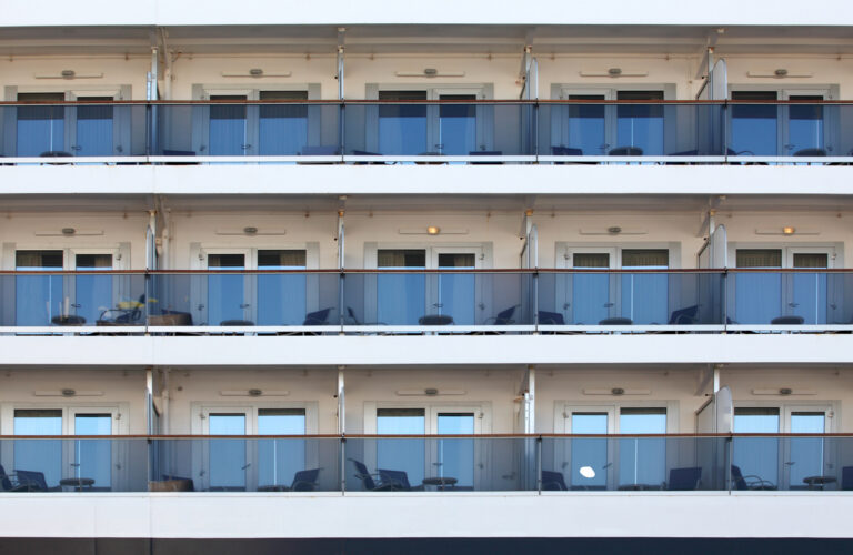 Row of cruise‑ship balcony staterooms with glass railings and outdoor seating arranged across multiple decks.