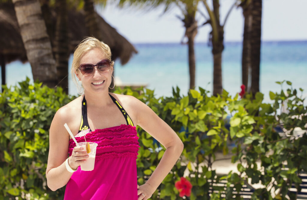 Person enjoying a tropical drink at a beach club with palm trees and ocean views in Cozumel.
