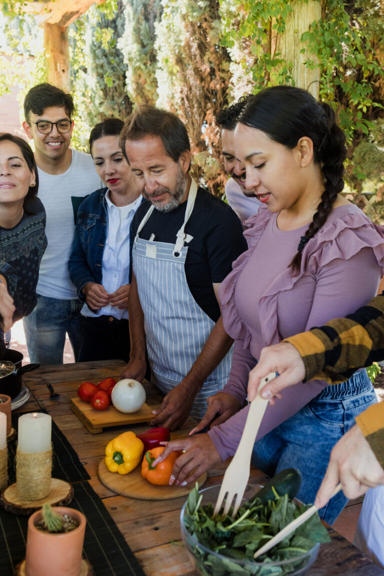 Group participating in an outdoor Mexican cooking class, preparing fresh vegetables at a wooden table.