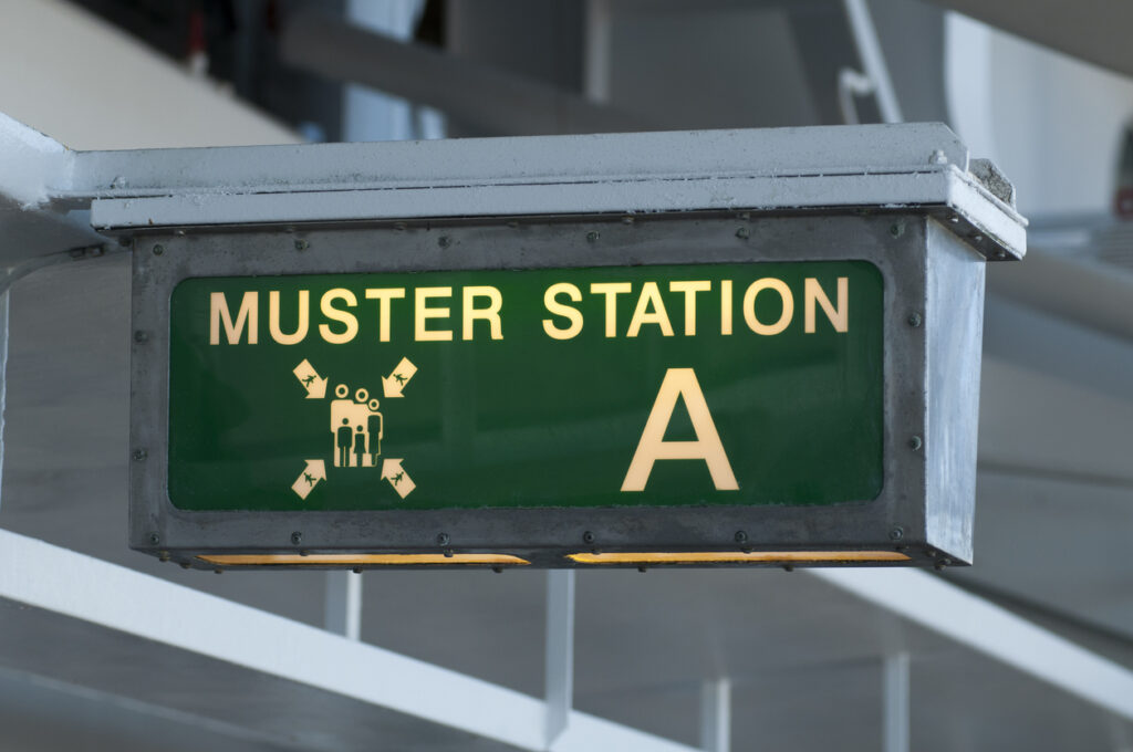 Cruise ship muster station area with signage showing where guests complete their safety check‑in.