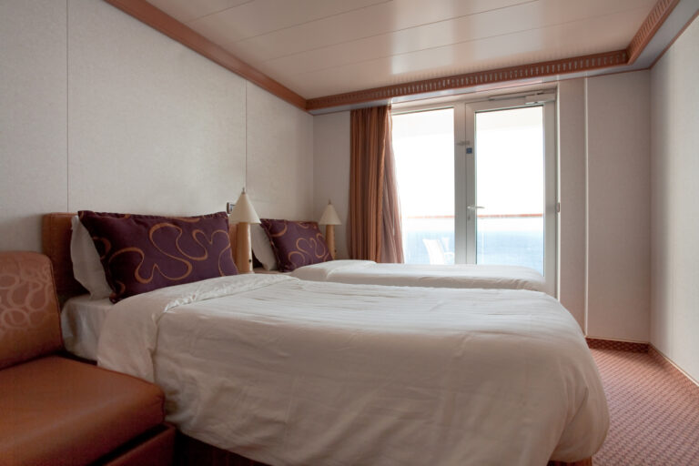 Cruise stateroom with neatly made bed and balcony light, showing a clean and organized room after housekeeping service.