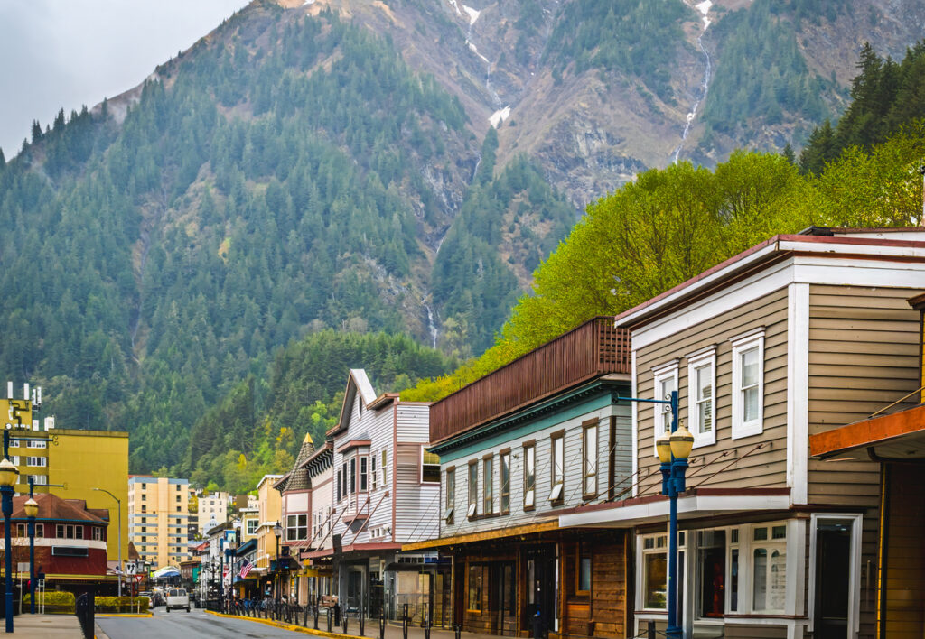 Colorful historic buildings along a downtown Juneau street with a forested mountain and waterfall rising behind them.