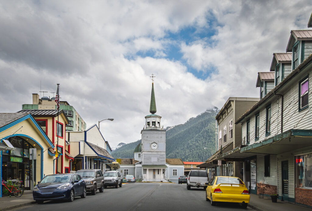 Historic Lincoln Street in downtown Sitka, Alaska, lined with shops and cafés in spring, with St. Michael’s Russian Orthodox Cathedral at the end of the street and mountains rising in the background.