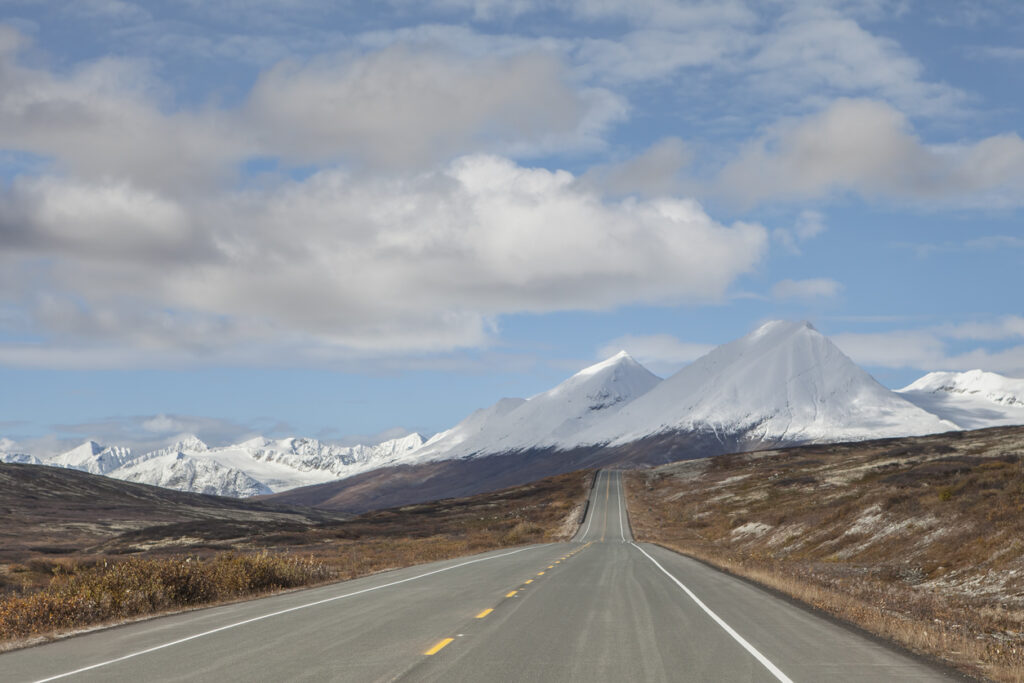 Scenic view of the Haines Highway stretching toward snow‑covered mountains in fall, showcasing the dramatic landscapes along the route from Haines, Alaska into British Columbia.