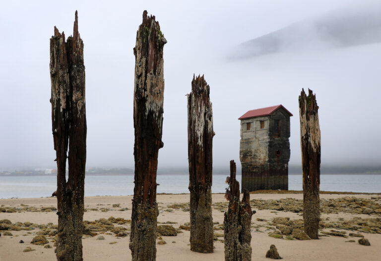 Weathered wooden pilings and an old concrete structure standing along the shoreline at the Treadwell Mine ruins in Juneau, Alaska.