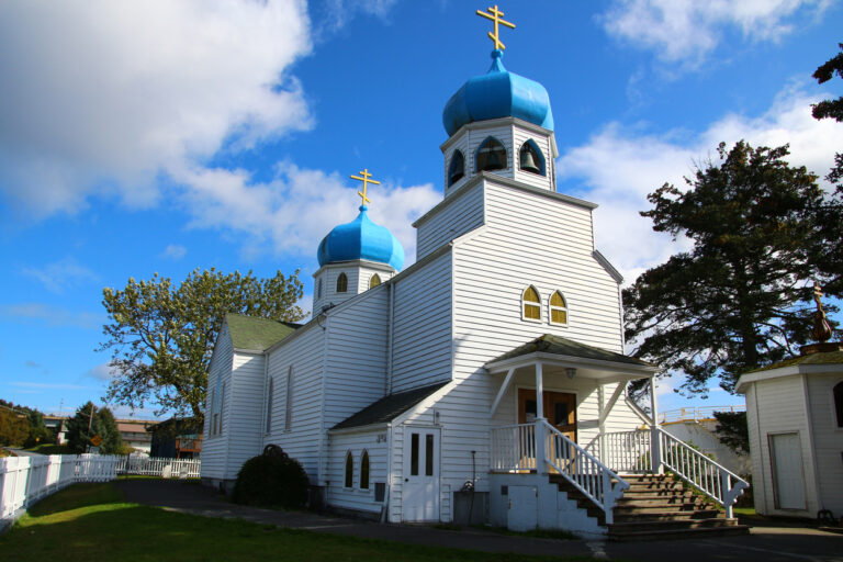 Exterior view of the Holy Resurrection Russian Orthodox Cathedral in Kodiak, Alaska, featuring its traditional domes and coastal setting.