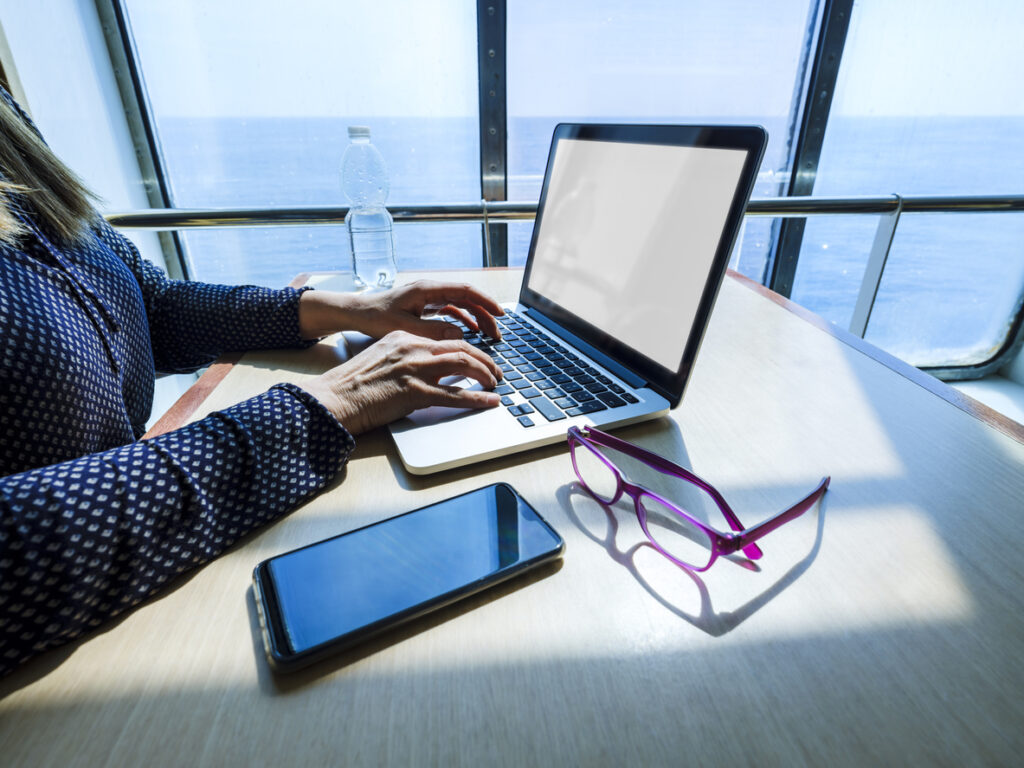 Person working on a laptop with an ocean view, illustrating practical ways to stay connected while learning how to save money on cruise wifi