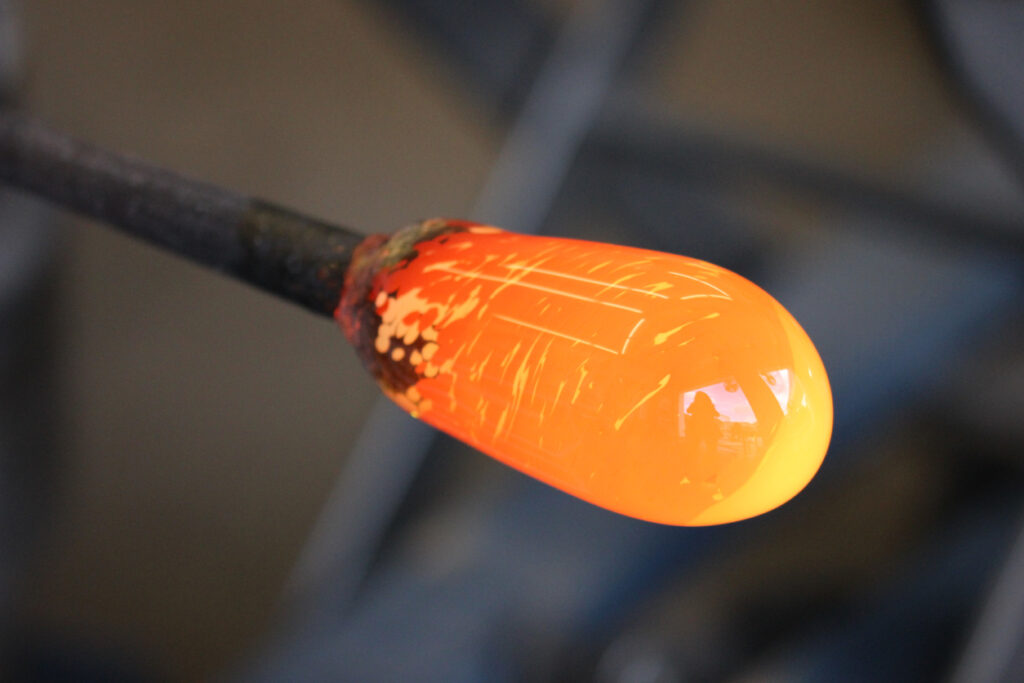 Molten glass glowing on the end of a rod during a glassblowing demonstration, shown in a close-up macro view.