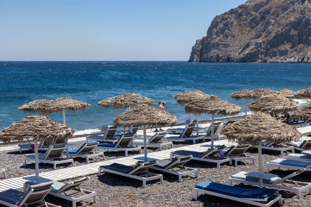 Sun loungers on the black volcanic beach of Kamari in Santorini. Cyclades, Greece