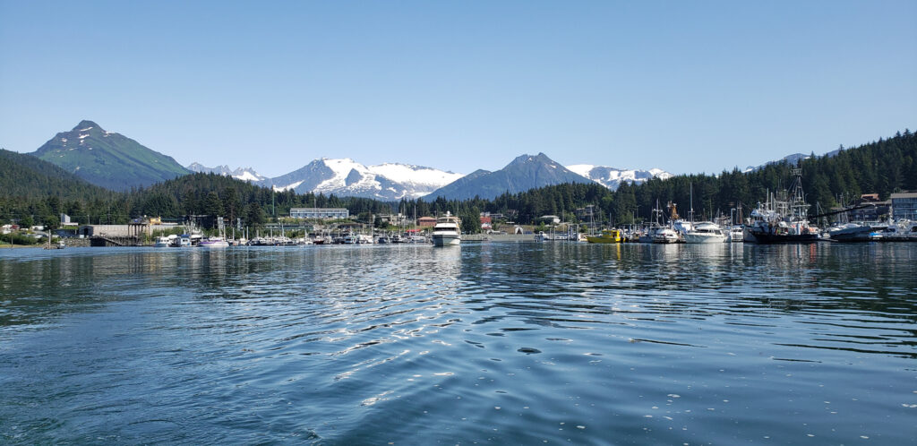 Harbor boats and calm water in Auke Bay with snow‑covered mountains and Mendenhall Glacier visible in the distance.