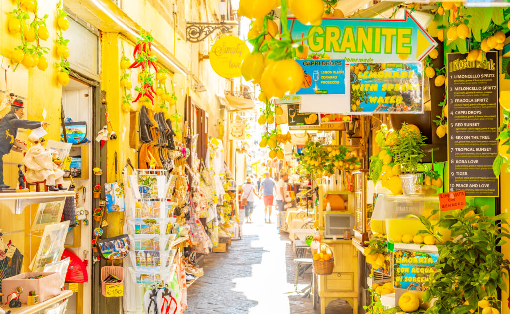 emon‑themed market street on Via San Cesareo in Sorrento’s old town, lined with souvenir stalls, hanging decorations, and shoppers walking through the narrow alley