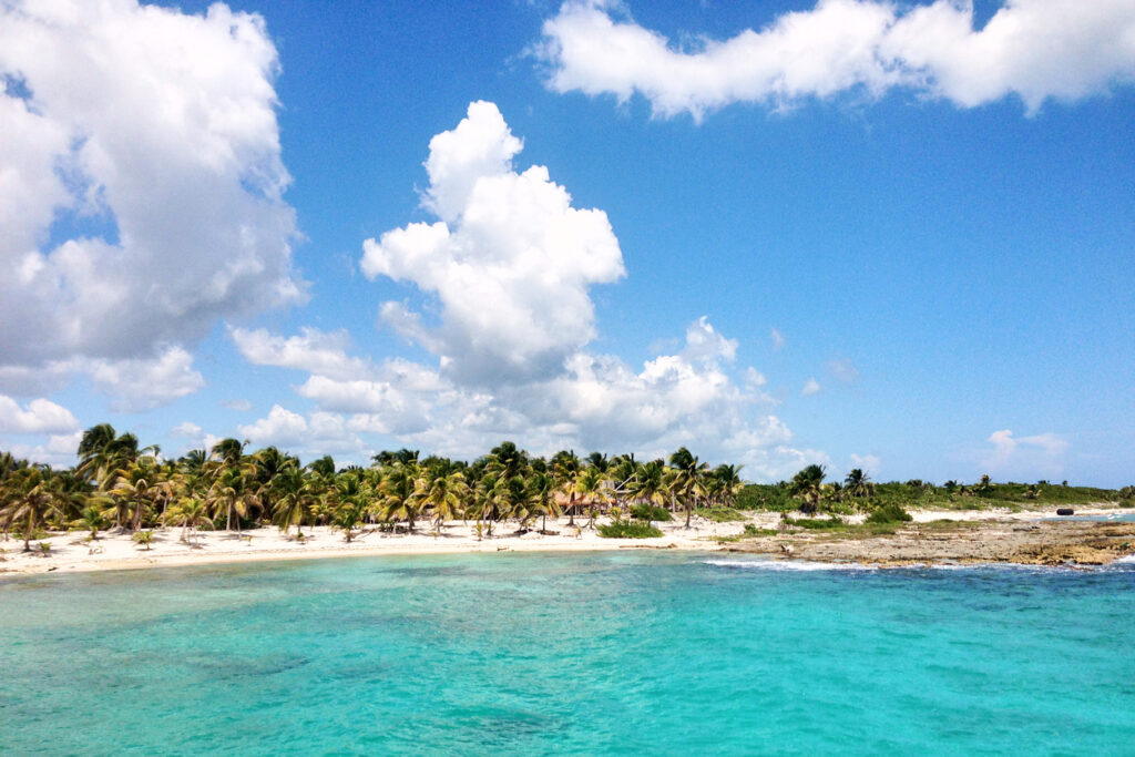 Calm turquoise water and soft sand along Mahahual Beach in Costa Maya, with beach chairs and palm trees creating a relaxed shoreline atmosphere.