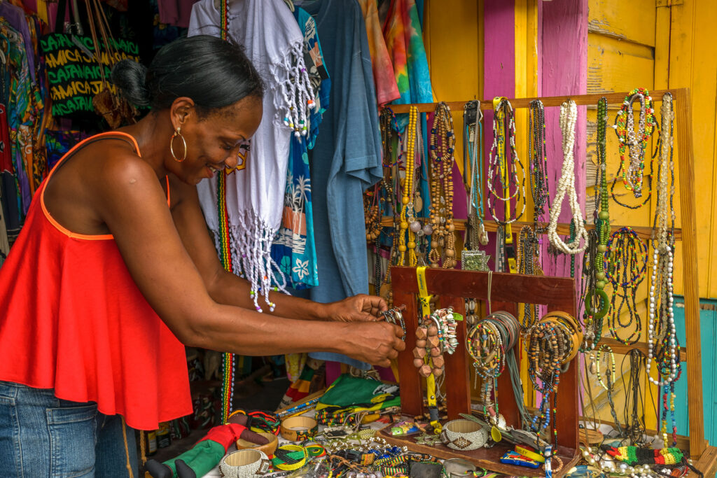Smiling Jamaican vendor displaying handmade bead chains, jewelry, and craft items at the Montego Bay Craft Market in Jamaica