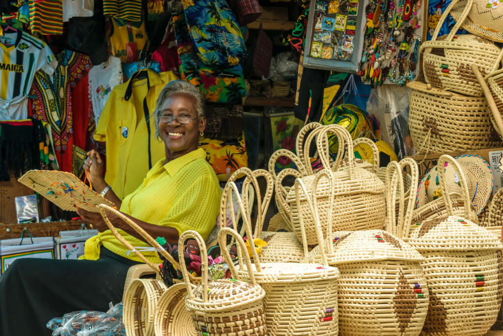 Smiling Jamaican vendor sitting in her stall surrounded by woven baskets and handmade crafts at the Montego Bay Craft Market in Jamaica