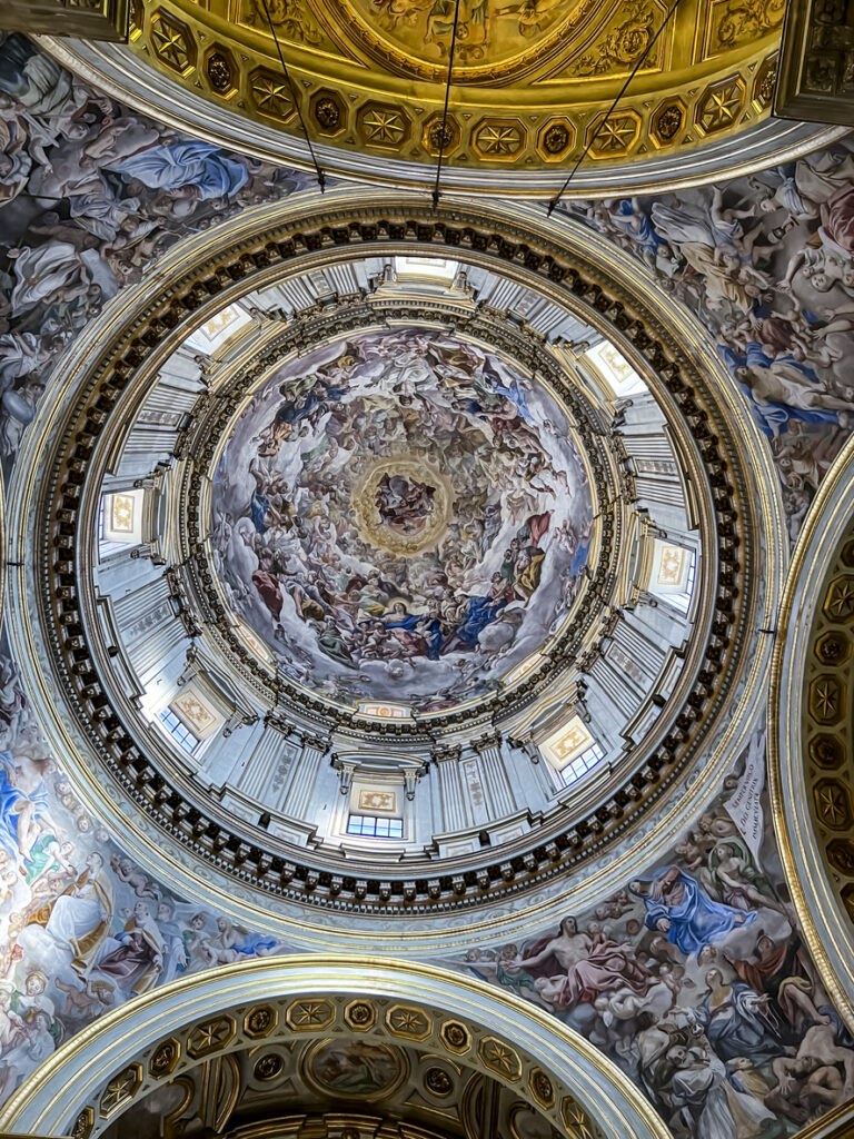 Richly decorated dome inside Naples Cathedral, featuring detailed frescoes, gold accents, and natural light illuminating the central artwork