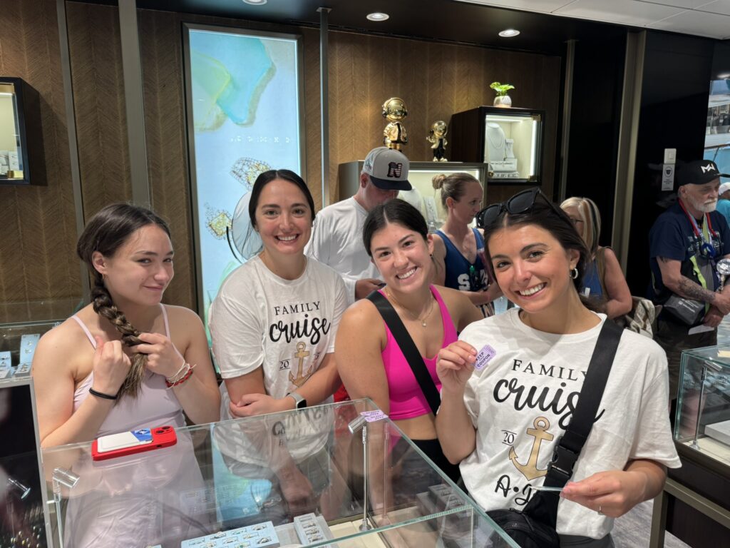 Guests browsing jewelry displays during an onboard shopping event, with one guest holding a Cruise Cash voucher inside the ship’s jewelry store.