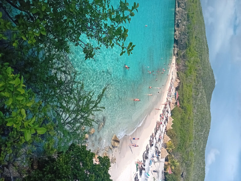 Aerial view of Playa Kenepa Grandi in Curaçao with bright turquoise water, high cliffs, and visitors swimming and relaxing on the beach