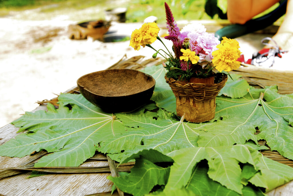 Rustic table arrangement with large green leaves, a woven basket of colorful flowers, and a natural wooden bowl at Rastafari Indigenous Village near Montego Bay, Jamaica