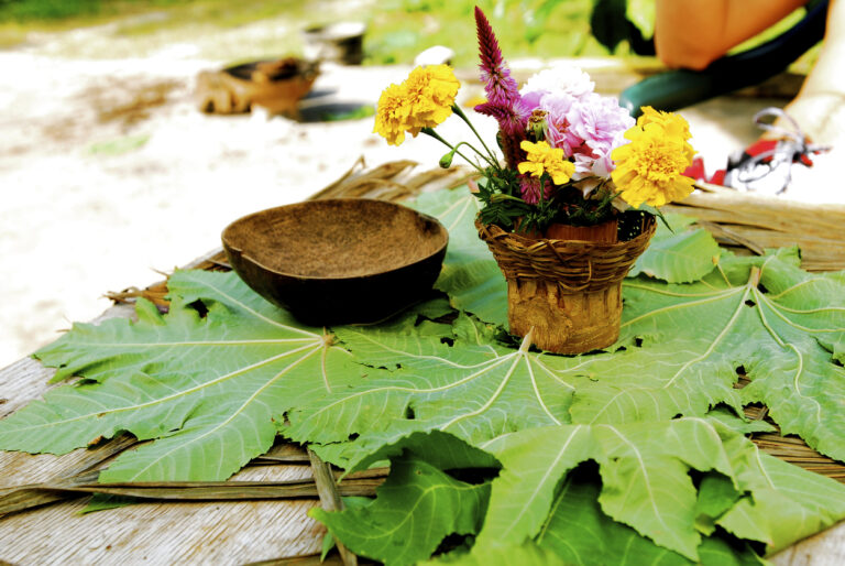 Rustic table arrangement with large green leaves, a woven basket of colorful flowers, and a natural wooden bowl at Rastafari Indigenous Village near Montego Bay, Jamaica