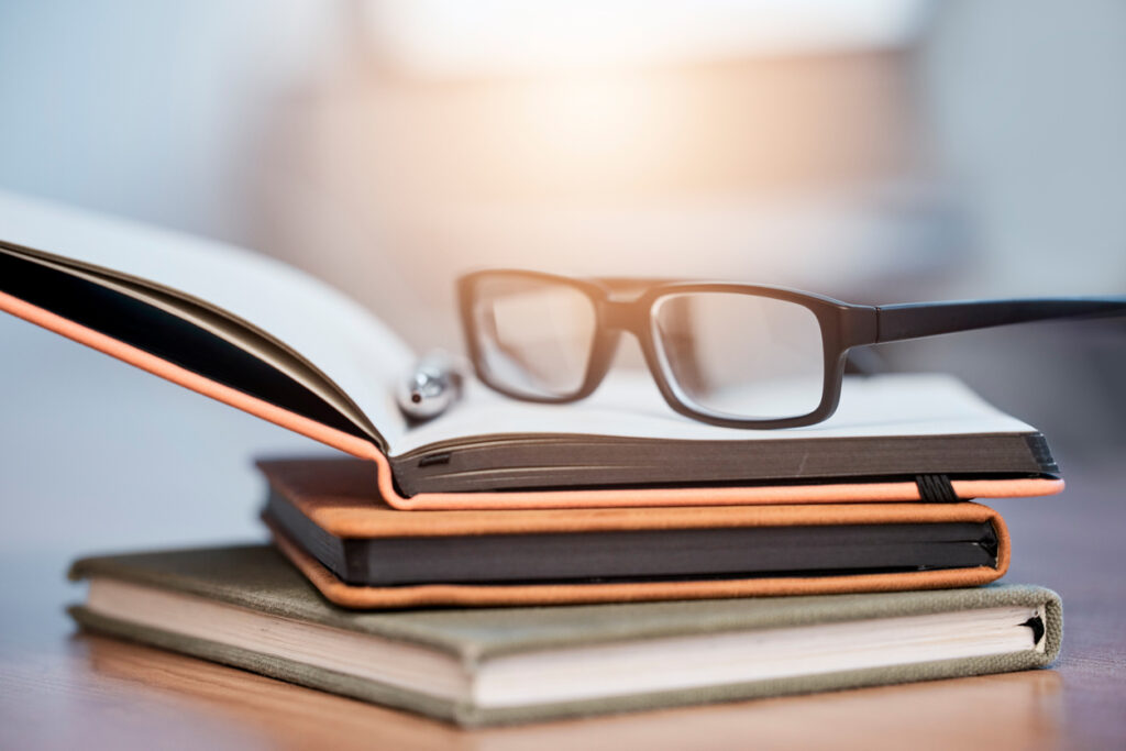 Close‑up of reading glasses resting on a small stack of books on a wooden table, creating a warm, library‑inspired scene.