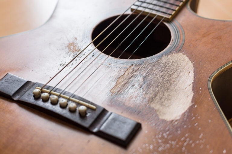 Selective focus on the worn wood and scratches of an old acoustic guitar, highlighting the character and history behind Jamaica’s musical roots
