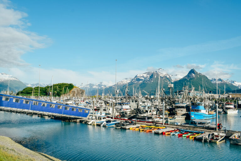 A rare sunny day at the Valdez Harbor in Alaska, with fishing boats and mountains reflected in the calm water.