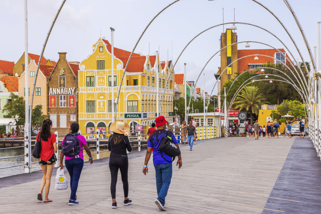 Tourists walking across the Queen Emma Bridge in Willemstad, Curaçao with colorful colonial buildings in the background