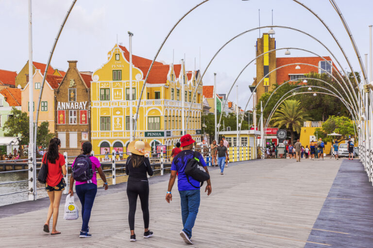 Tourists walking across the Queen Emma Bridge in Willemstad, Curaçao with colorful colonial buildings in the background