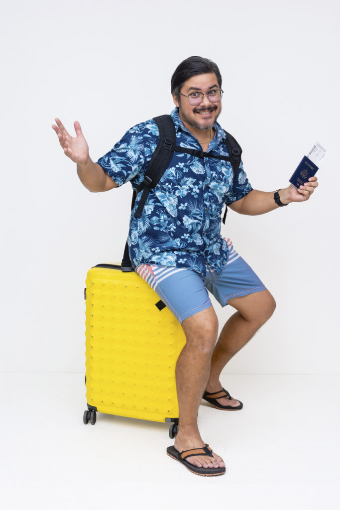 Traveler sitting on a yellow suitcase holding a passport and boarding pass, ready for embarkation day, illustrating items from a cruise carry‑on checklist.